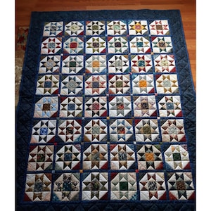 May include: A handmade quilt with a navy blue border and backing. The quilt features a repeating pattern of star blocks in various colors, including red, green, yellow, and blue. The quilt is approximately 70 inches by 80 inches.