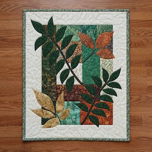 May include: A rectangular quilted wall hanging featuring a central block design of green, brown, and orange fabric patches. The quilt is decorated with appliquéd leaf branches in dark green, golden yellow, and burnt orange, framed by a cream border.