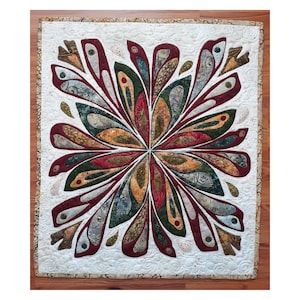 May include: A handmade quilt with a central floral design. The quilt features a symmetrical pattern of burgundy, green, and gold petal-like shapes against a white background. The edges are bordered with a patterned fabric, showcasing a blend of colors and textures.