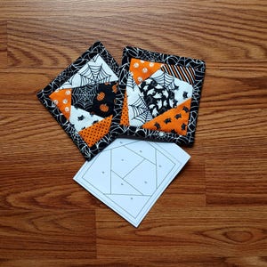 May include: Two Halloween-themed quilted coasters with black spiderweb and pumpkin patterns, and a paper template. The coasters feature orange, black, and white fabrics. The coasters are square and have a black border with a spiderweb design.