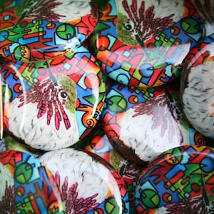 May include: A collection of colorful round buttons featuring a hummingbird design. The buttons have a geometric pattern with red, blue, green, and white colors. The hummingbird is depicted in a realistic style with detailed feathers and a long beak.