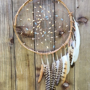 May include: A brown dreamcatcher with white and blue beads and feathers hanging from the bottom. The dreamcatcher is hanging on a wooden wall.