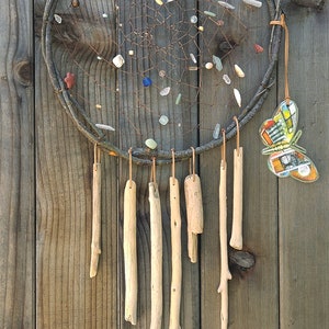 May include: A brown twig dreamcatcher with a white and brown butterfly charm hanging from the bottom. The dreamcatcher is decorated with various colored beads and stones.