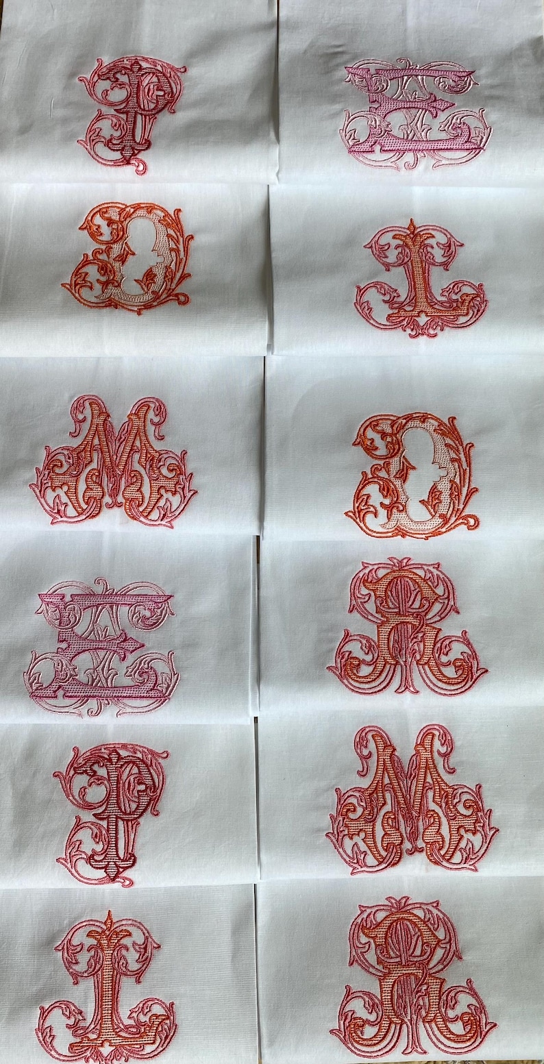 May include: A collection of white fabric squares, each featuring a distinct, ornate embroidered letter in shades of pink and orange. The letters are rendered in a decorative, swirling script style, centered on each individual white textile piece.