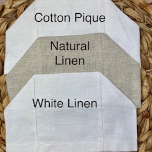 Op de afbeelding: Drie stoffen stalen verticaal gerangschikt. De bovenste staal is wit katoen piqu&eacute; met een geweven textuur. De middelste staal is beige natuurlijk linnen. De onderste staal is wit linnen. Elk stuk heeft een gevouwen, hoekige bovenrand.