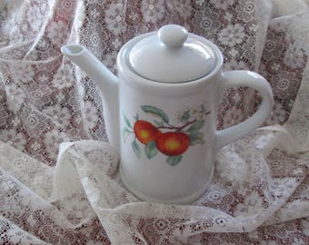 May include: White ceramic teapot with a lid and a handle. The teapot features a floral design with red apples.