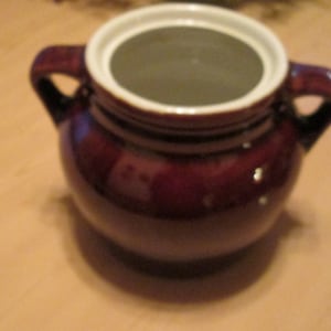 Könnte beinhalten: Ein brauner Keramiktopf mit einem weißen Deckel und zwei Griffen. Der Topf hat eine glasierte Oberfläche und ist mit einem dezenten Muster verziert.