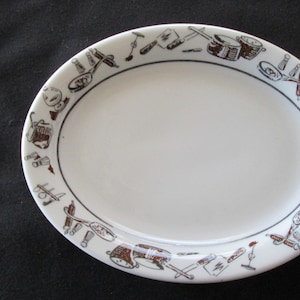 以下が含まれることがあります： 茶色と黒の縁取りのデザインが施された白い楕円形のセラミックプレート。様々なキッチン用品が描かれています。