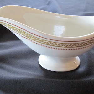 以下が含まれることがあります： 金と赤の装飾的な縁取りが施された白い陶器製のグレービーボート。ボートにはハンドルと台座があります。