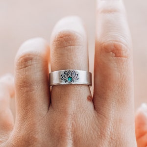 May include: A silver ring with a lotus flower design and a turquoise stone in the center.