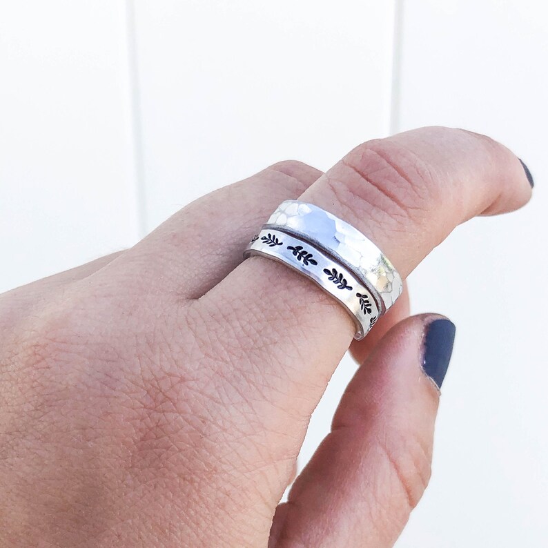 Puede incluir: Dos anillos de plata apilados en un dedo. El anillo superior tiene un acabado martillado. El anillo inferior tiene un delicado dise&ntilde;o de hojas.