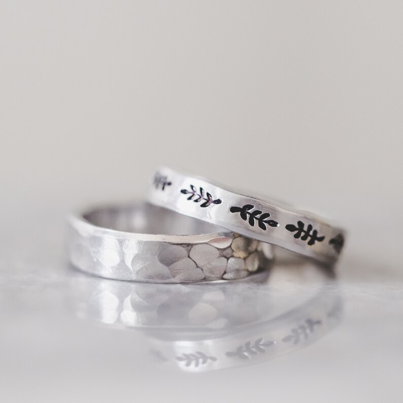 Puede incluir: Dos anillos de plata, uno con textura martillada y el otro con un delicado dise&ntilde;o de hojas. Los anillos est&aacute;n apilados uno encima del otro.