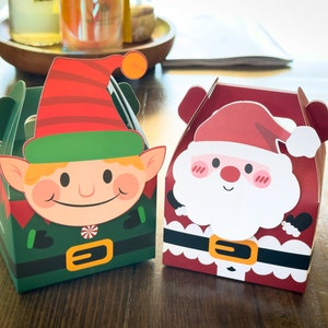 May include: Two Christmas-themed gift boxes, one with a green elf and the other with a red Santa Claus. Both boxes have a handle on top.