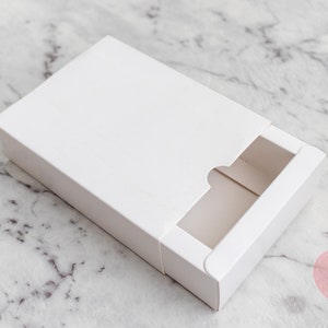 May include: A white cardboard box with a sliding drawer. The drawer has a cut-out opening on the front.