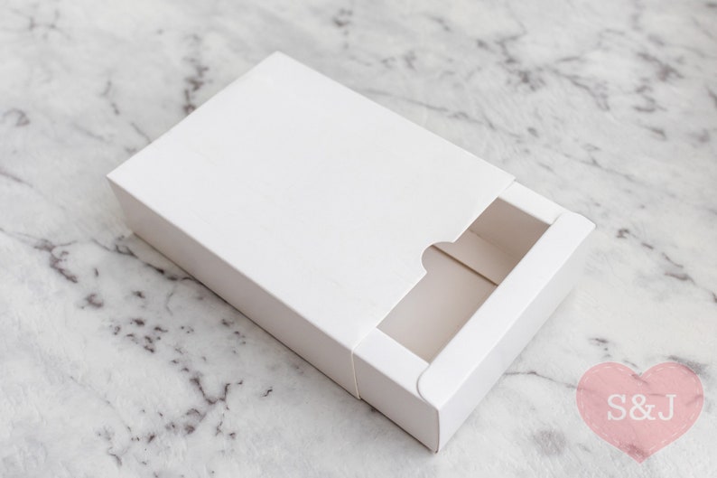 May include: A white cardboard box with a sliding drawer. The drawer has a cut-out opening on the front.