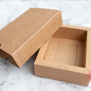 May include: A brown cardboard box with a lid. The box is open and the lid is lying next to it. The box is empty.