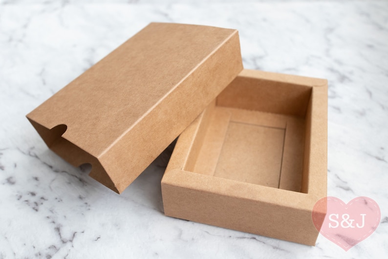 May include: A brown cardboard box with a lid. The box is open and the lid is lying next to it. The box is empty.