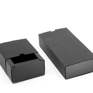 May include: Two black cardboard boxes, one open and one closed. The open box has a drawer-like lid that is partially open. The boxes are both rectangular and have a smooth, matte finish.