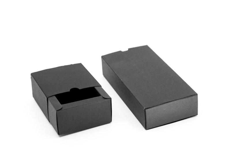 May include: Two black cardboard boxes, one open and one closed. The open box has a drawer-like lid that is partially open. The boxes are both rectangular and have a smooth, matte finish.