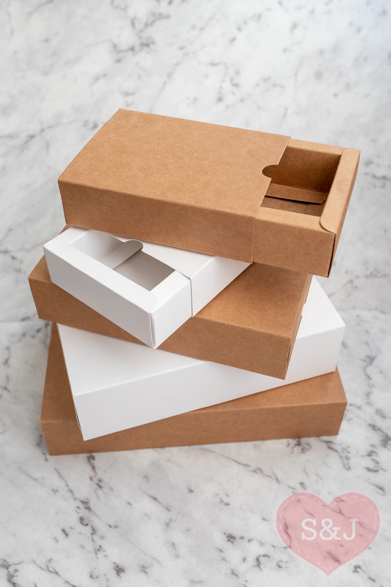 May include: Four cardboard boxes stacked on top of each other. The top box is brown with a cut-out window. The second box is white with a cut-out window. The third box is brown and the bottom box is brown.
