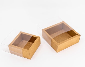 May include: Two brown cardboard boxes with clear plastic lids. The boxes are empty and are sitting on a white surface.