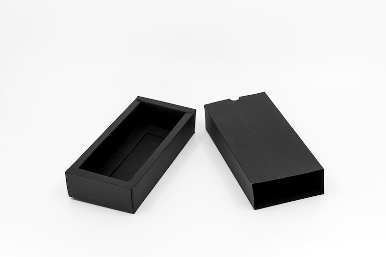 May include: A black rectangular box with a lid, open to reveal an empty interior. The box is made of cardboard and has a smooth, matte finish.