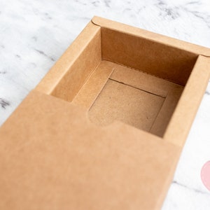 May include: A brown cardboard box with a sliding lid. The box is open and the inside is empty.