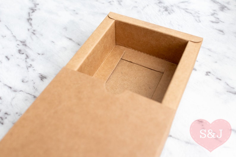 May include: A brown cardboard box with a sliding lid. The box is open and the inside is empty.
