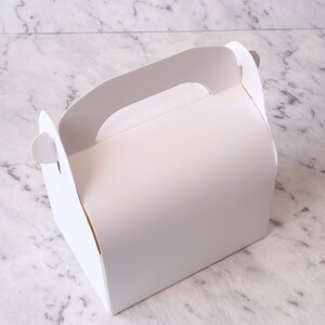 K&ouml;nnte beinhalten: Wei&szlig;e Pappbox mit Griff, perfekt zum Verpacken von kleinen Geschenken oder Leckereien.