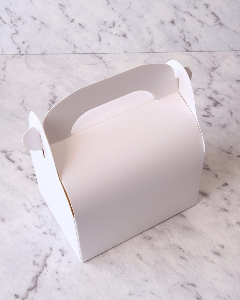 K&ouml;nnte beinhalten: Wei&szlig;e Pappbox mit Griff, perfekt zum Verpacken von kleinen Geschenken oder Leckereien.
