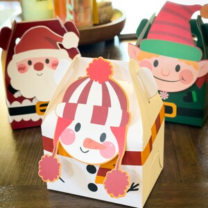 May include: Three Christmas-themed gift boxes with a snowman, Santa Claus, and an elf design. The boxes are made of cardboard and have a festive red, green, and white color scheme.