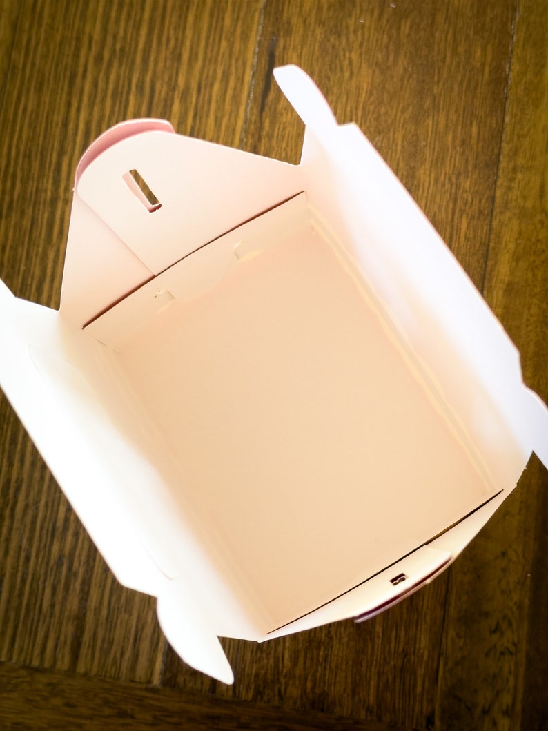 May include: A white cardboard takeout box with a pink interior. The box is empty and open, showing the inside.