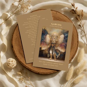 May include: Two tarot cards featuring the Garuda, a winged protector. One card displays the Garuda with colorful wings and the text "YOU ARE CARRIED ABOVE WHAT SEEKS TO BIND YOU." The other card has text about the Garuda.