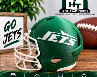 Puede incluir: Un casco de fútbol americano verde con el logotipo blanco de los Jets en el lateral y una máscara facial blanca. El casco tiene un acabado texturizado e incluye aberturas de ventilación. Es una réplica de un casco deportivo decorativo.