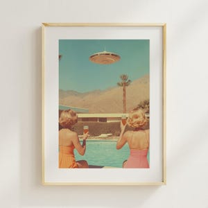 May include: Two people in swimsuits sit by a pool, looking up at a flying saucer in the sky. They are holding glasses of a light-colored beverage. The pool is surrounded by palm trees and a desert landscape.