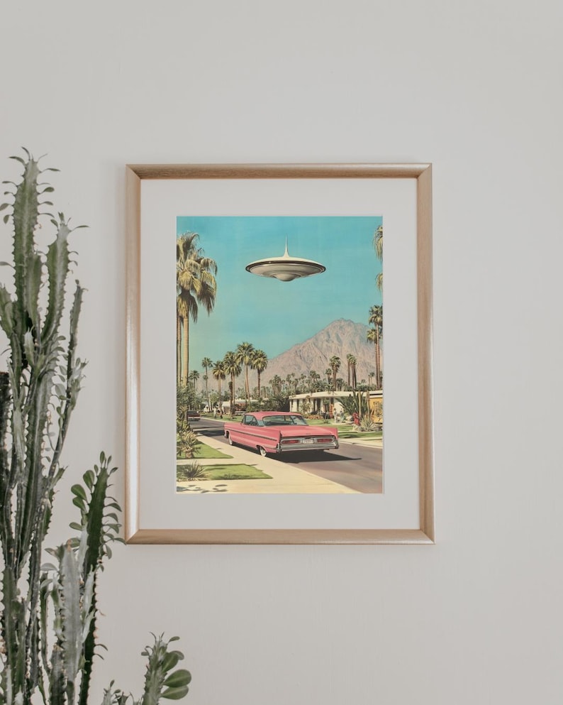 May include: A framed print of a pink car driving down a palm tree lined street with a flying saucer in the sky.