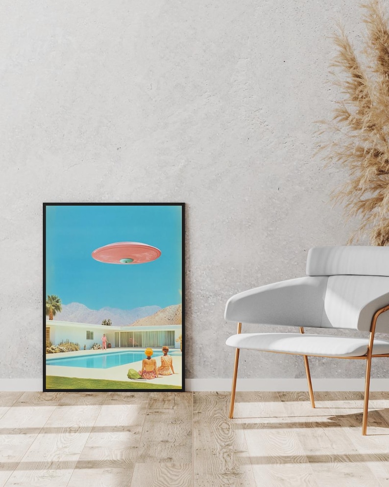 May include: A framed print of a mid-century modern home with a swimming pool and two people in bathing suits. A pink flying saucer is hovering over the house.