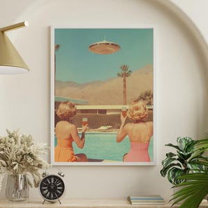May include: Two women in swimsuits sit by a pool, looking up at a flying saucer in the sky. They are each holding a glass of a light-colored beverage. The scene is set against a desert landscape with palm trees and a blue sky.