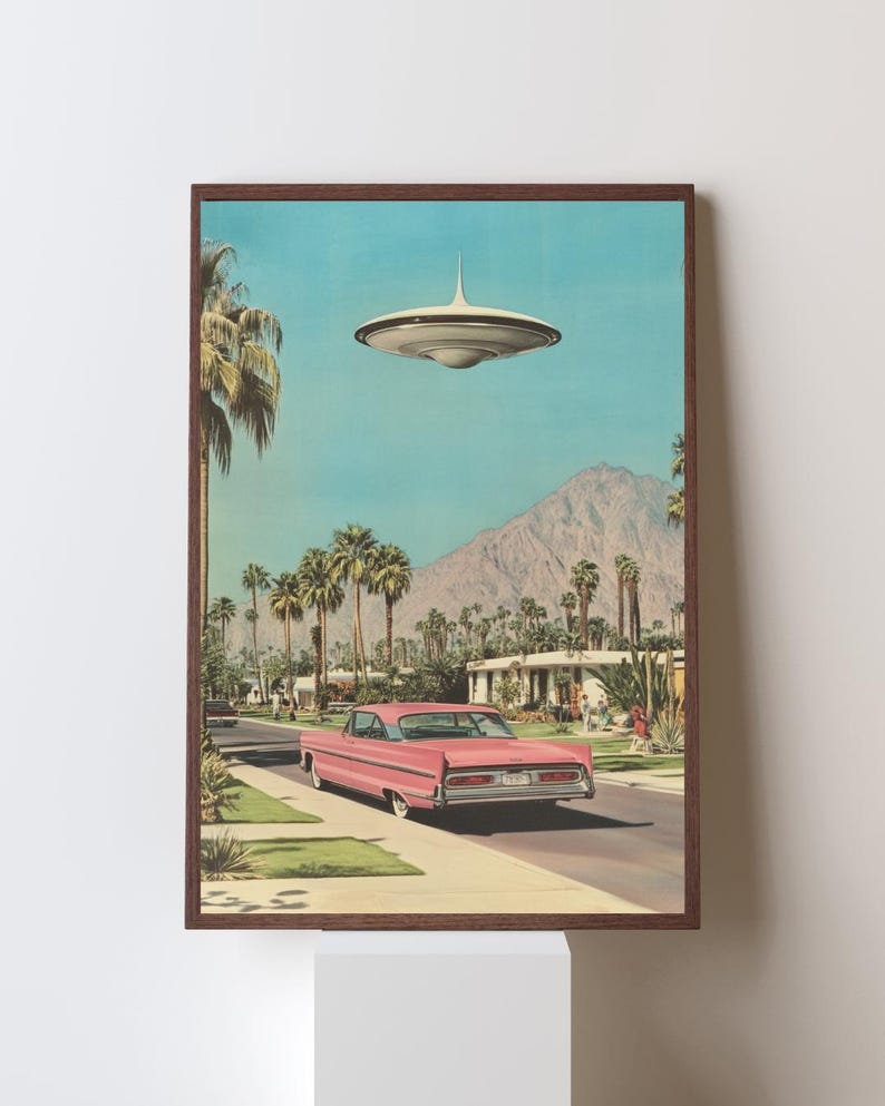 May include: A pink vintage car drives down a palm tree lined street in a desert town. A flying saucer hovers above the car.