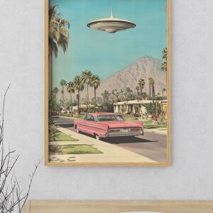 May include: A pink vintage car drives down a suburban street with palm trees and a mountain in the background. A flying saucer hovers above the street.