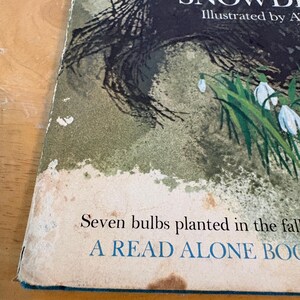 May include: Vintage book cover featuring the title "Cindy's Snowdrop" with illustrations. The cover art includes a dark, textured illustration and a cluster of white snowdrop flowers. The text "Seven bulbs planted in the fall" is also visible.