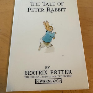 May include: A vintage copy of "The Tale of Peter Rabbit" by Beatrix Potter. The cover features an illustration of Peter Rabbit in a blue jacket. The title and author's name are printed in black, with the publisher's logo at the bottom.
