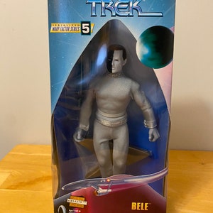 May include: A Star Trek action figure of the character 'B'Elanna Torres' from the television series Star Trek: Voyager. The figure is wearing a silver jumpsuit and has a black and white face. The figure is packaged in a box with the Star Trek logo and the number 5. The box also includes the words 'Serialized Warp Factor Series' and 'Limited Edition'.