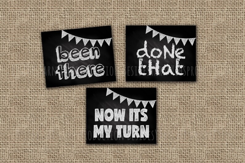 May include: Three black chalkboard signs with white chalk lettering and a string of white chalk flags hanging above each sign. The signs read "been there", "done that", and "now its my turn".