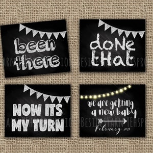 May include: Four black chalkboard signs with white text announcing a new baby. The signs read "been there", "done that", "now it's my turn", and "we are getting a new baby, February 2017".