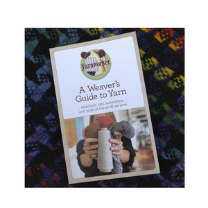 May include: A book titled "A Weaver's Guide to Yarn: selection, size, substance, and style of the stuff we love" by Liz Gipson. The book cover features a photo of a person holding different types of yarn.