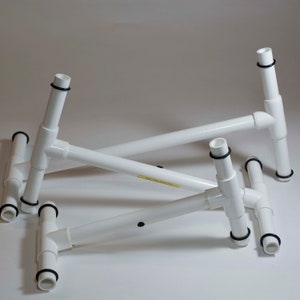 May include: Three white plastic T-shaped stands with black rubber rings at the ends of each leg. The stands are stacked on top of each other.
