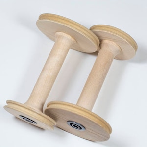 May include: Two wooden yarn swift spools with a natural finish. The spools are made of wood and have a smooth surface. The spools are designed to hold yarn for spinning or knitting.