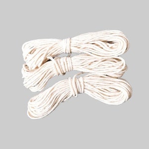 May include: Three spools of white cotton twine, each wound tightly and ready for use in crafting or other projects.