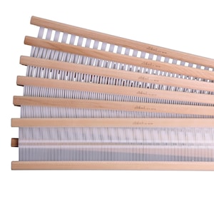 May include: A set of six wooden weaving heddles with white warp threads. The heddles are stacked on top of each other and labeled " Ashford, 10/20"